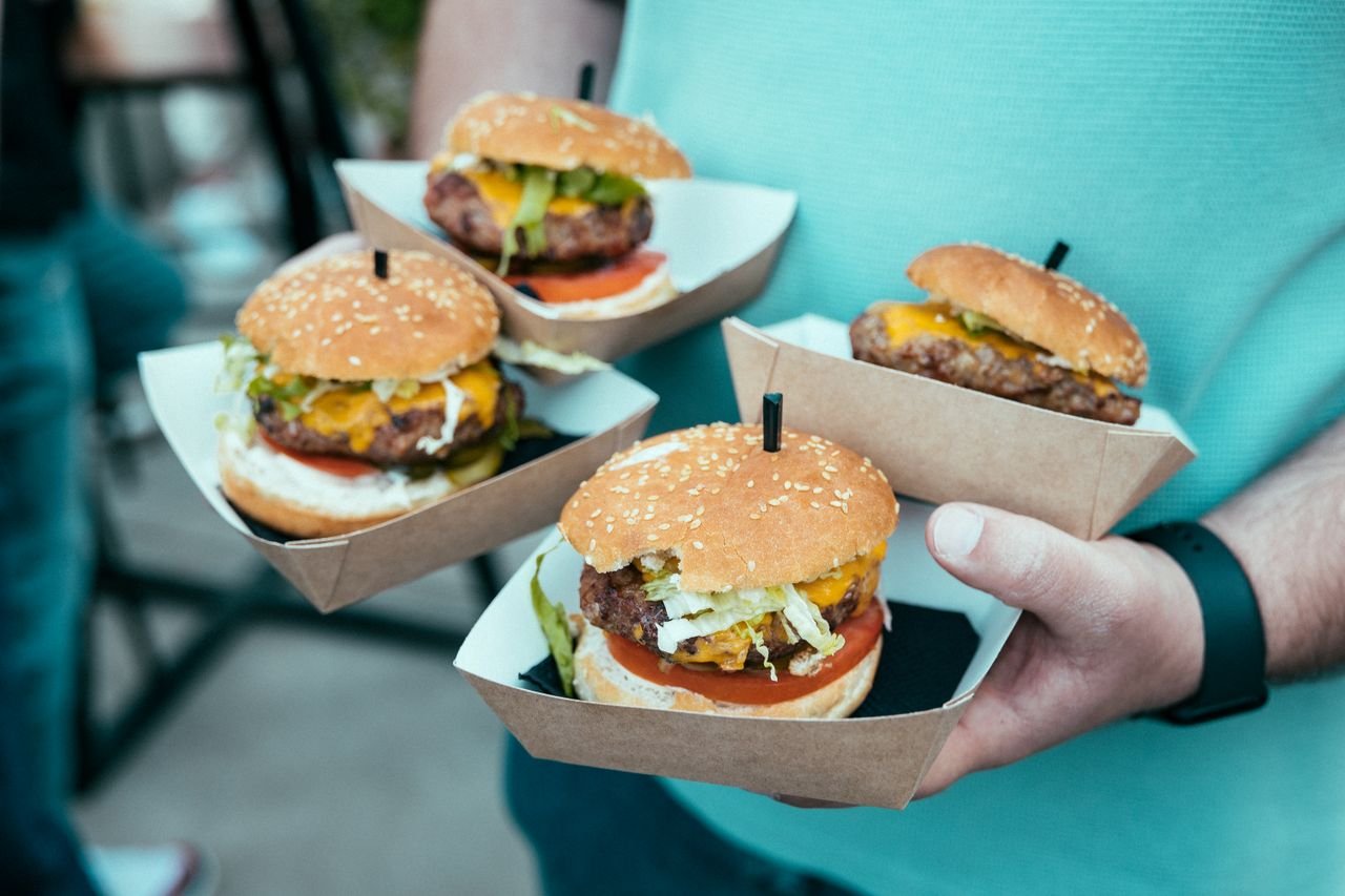 Home A close-up of hands holding four juicy beef burgers in cardboard trays, ideal for food lovers.