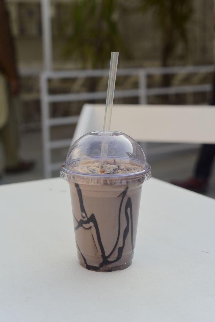 Home Delicious chocolate milkshake in a plastic cup on a table outdoors, perfect for a summer refreshment.