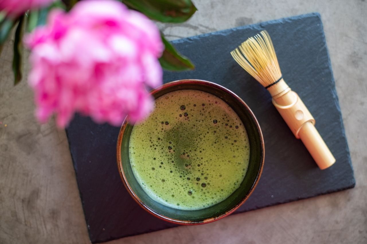Home A top-down view of matcha tea and pink peonies, embodying simple beauty and relaxation.