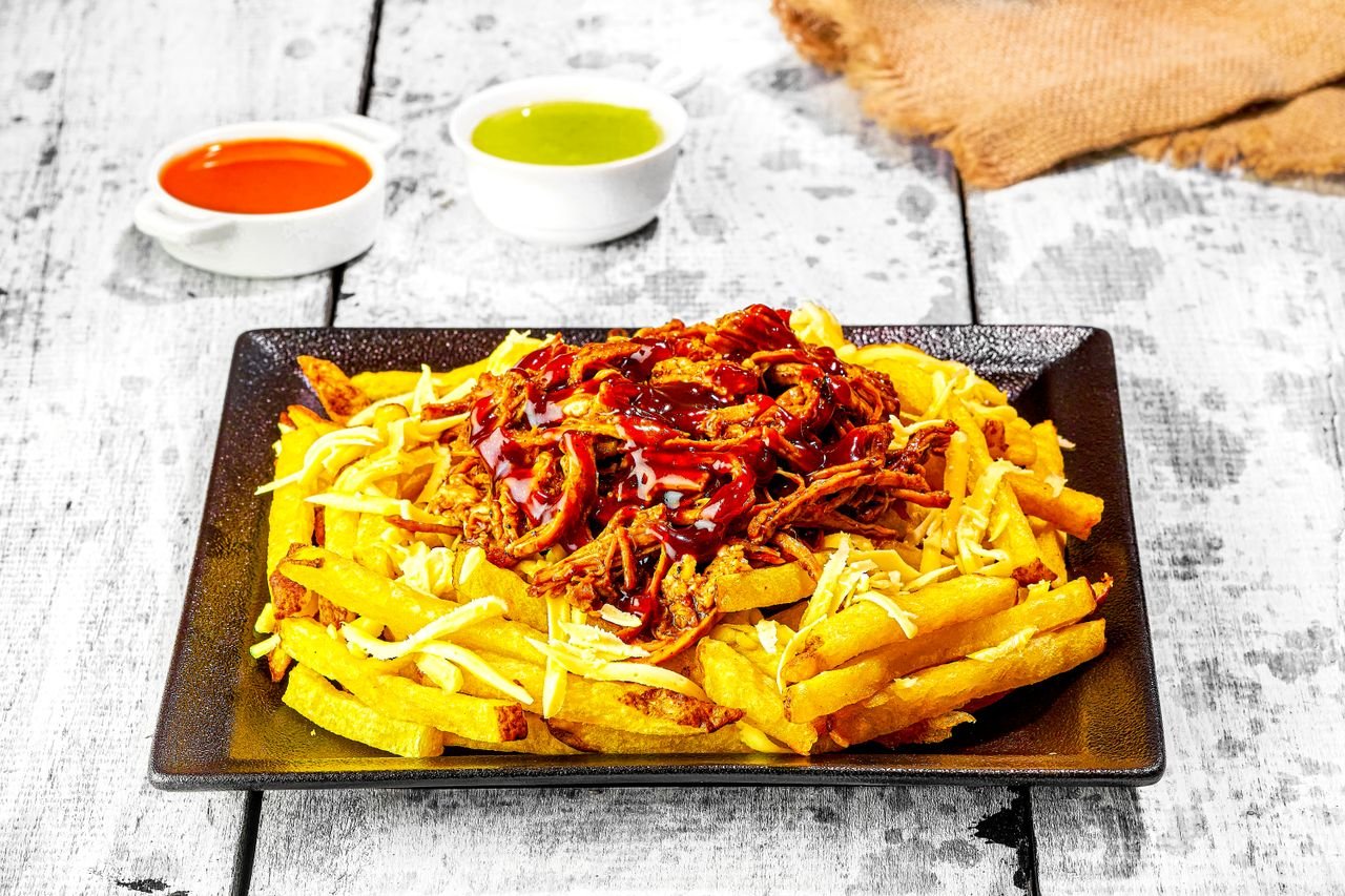 Home Tasty loaded fries topped with BBQ pulled pork, cheese, and sauces served on a rustic table.